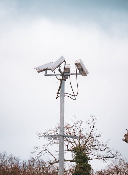 Outdoor security cameras mounted on a tall metal pole against a cloudy sky, ensuring surveillance.